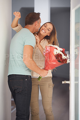 Buy stock photo Husband, gift and flowers for wife by front door, hug and happy couple to celebrate love in home. Man, care and grateful with floral present for woman, gratitude and bonding together on anniversary