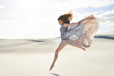 Buy stock photo Side view of a beautiful young woman in a flowing dress jumping across sand