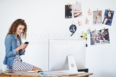 Buy stock photo Shot of a young woman using a cellphone while sitting on her desk in an office