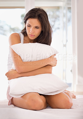 Buy stock photo A young woman looking unhappy whiile hugging her pillow