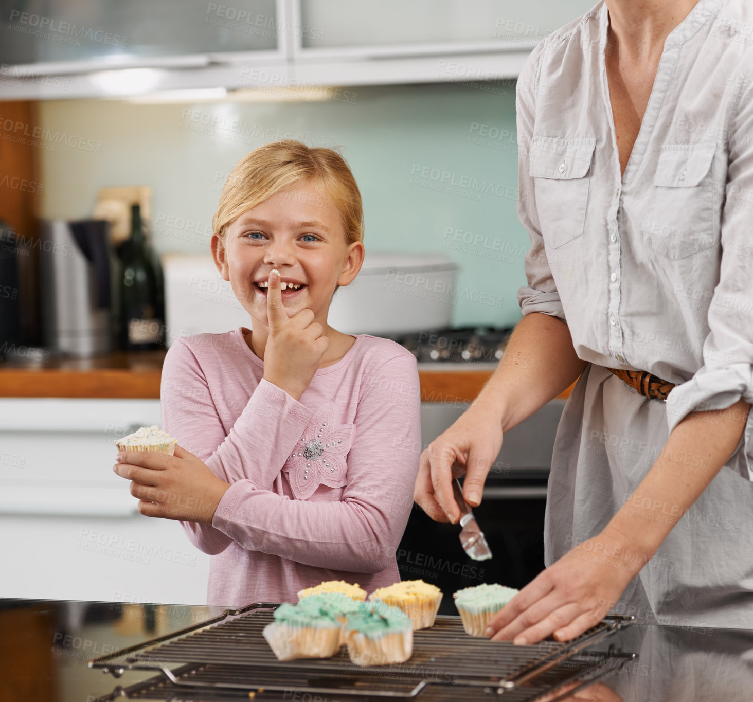 Buy stock photo Portrait of an adorable little girl helping her mom frost cupcakes in the kitchen