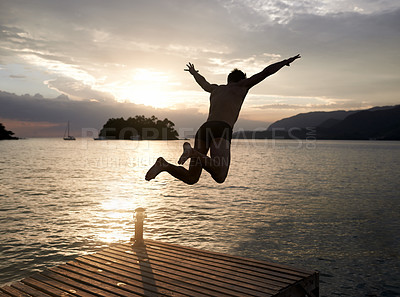 Buy stock photo Rear view shot of a young man diving off the jetty into a lake at sunset