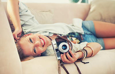 Buy stock photo Portrait of a beautiful young woman holding her camera while lying on a couch