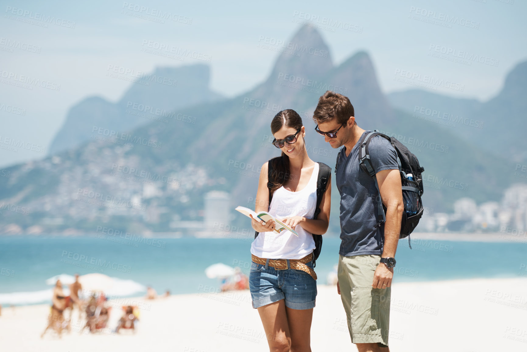 Buy stock photo Shot of a young couple looking at a map while standing on a beach