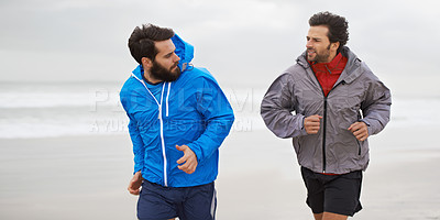 Buy stock photo Cropped shot of two young men jogging together along the beach on an overcast morning