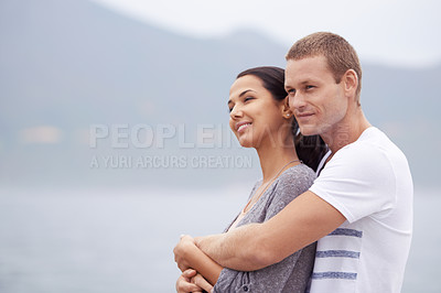 Buy stock photo Shot of a handsome young man affectionately embracing his girlfriend at the beach