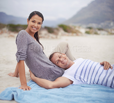 Buy stock photo Shot of a handsome young man lying on his girlfriend's lap at the beach