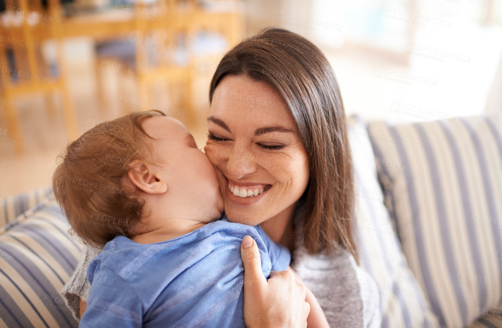 Buy stock photo Mother, baby and kiss for love in embrace, care and support or relax in living room and comfortable. Mommy, son and affection for bonding in childhood, security and happiness in hug or smile on face