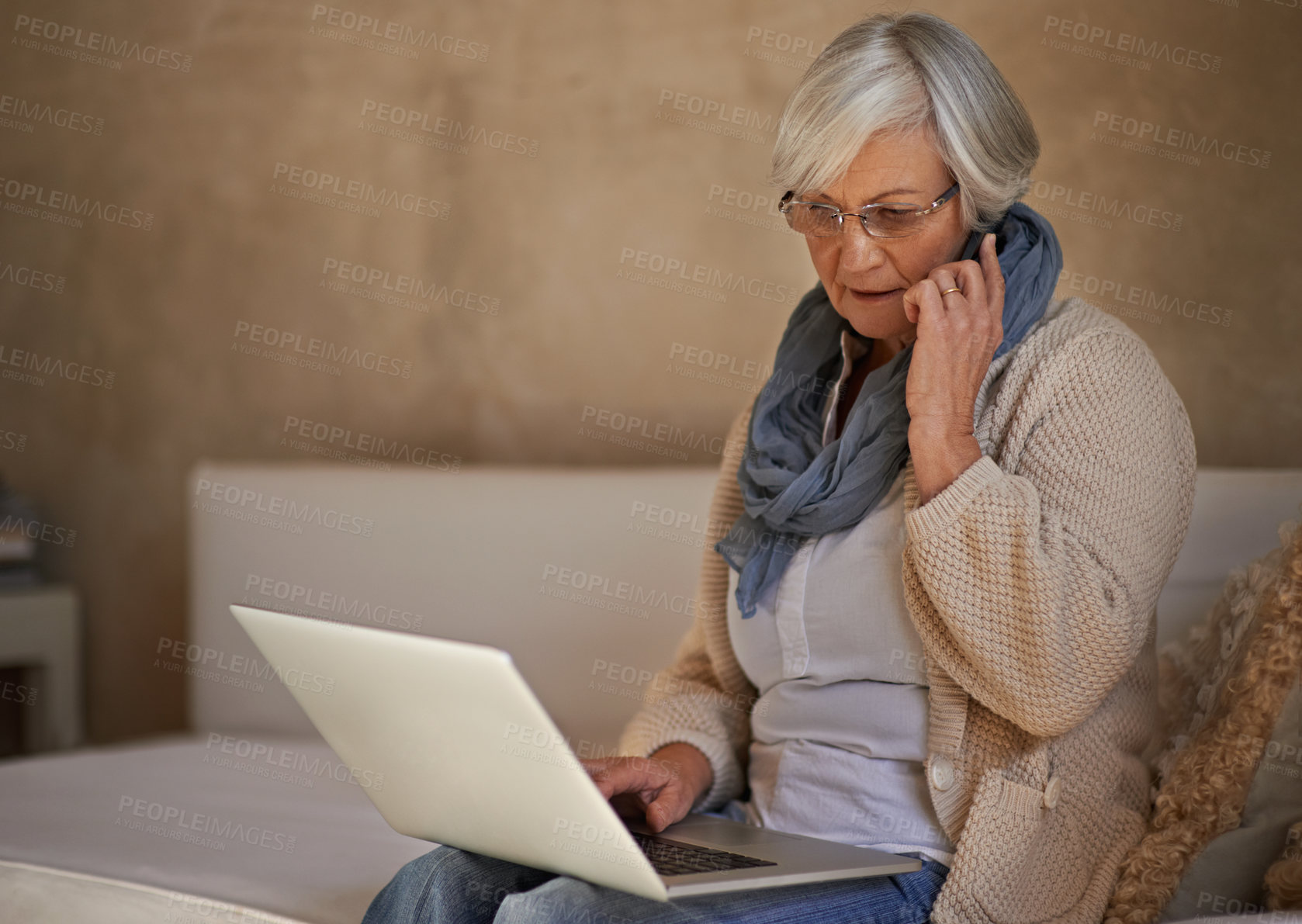 Buy stock photo A senior woman on her mobile while using her laptop at home