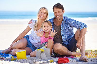 Buy stock photo Parents, girl and sandcastle in portrait at beach, blanket and excited with hug for holiday in summer. Father, mother and daughter with picnic by ocean for vacation in nature with love in sunshine