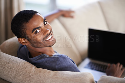 Buy stock photo Cropped shot of a handsome young man using his laptop while relaxing at home