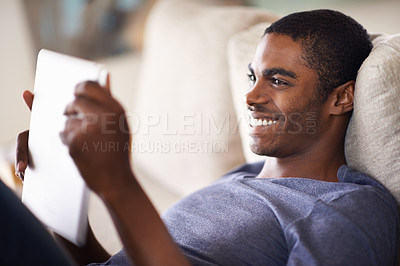 Buy stock photo Cropped shot of a handsome young man using his tablet while relaxing at home