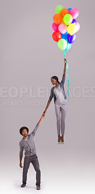 Buy stock photo Balloon, float and couple in studio for birthday, celebration and present on gray background. Trust, flying and isolated man and woman holding hands with inflatable for party, gift and surprise