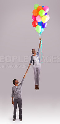 Buy stock photo Balloon, flying and couple in studio for growth, celebration and present on gray background. independant, opportunity and isolated man and woman holding hands with inflatable for party and surprise