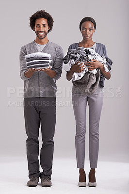 Buy stock photo People, studio and pile of washing in hand for wash, laundry day and couple cleaning together. Happy, man and neat clothes folded with woman, messy and unhappy for dirty wardrobe on gray background