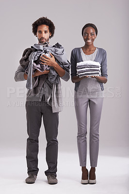 Buy stock photo Portrait, studio and people with pile of clothes in hand for laundry day, wash or cleaning together. Woman, smile and  washing folded with messy, man and annoyed for dirty wardrobe on gray background