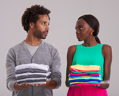 Buy stock photo Couple, folded clothes and laundry in studio for chores, domestic and housework together. Black people, man and woman in relationship or married are organizing, color code shirts on gray background