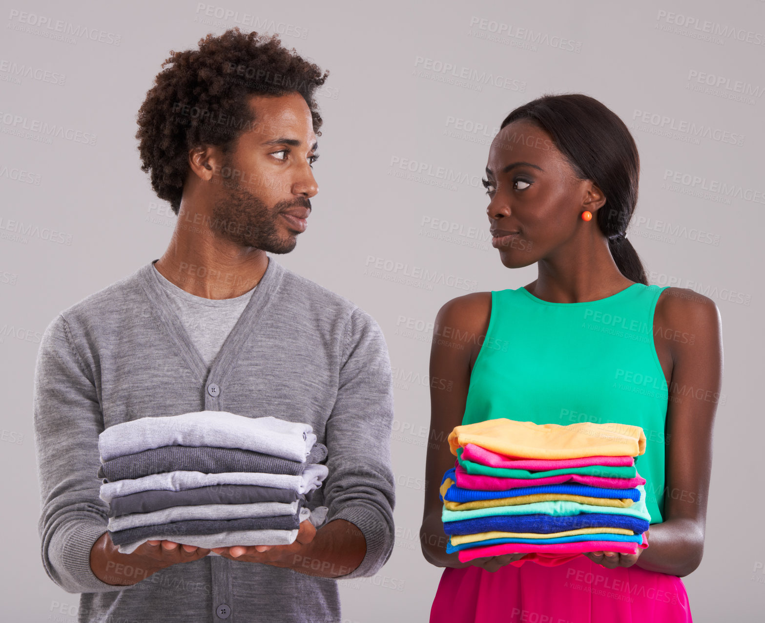 Buy stock photo Couple, folded clothes and laundry in studio for chores, domestic and housework together. Black people, man and woman in relationship or married are organizing, color code shirts on gray background