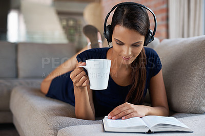 Buy stock photo Shot of a beautiful young woman relaxing on her couch with music and a good book