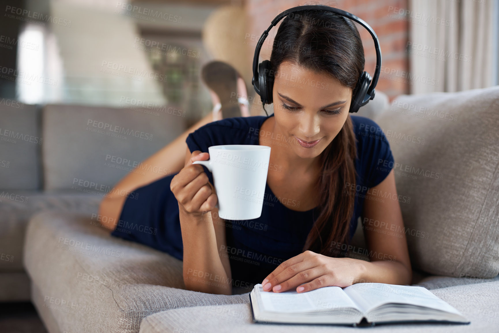 Buy stock photo Shot of a beautiful young woman relaxing on her couch with music and a good book