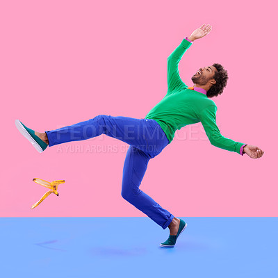 Buy stock photo Humorous shot of a young man slipping on a banana peel agains a colorful studio background