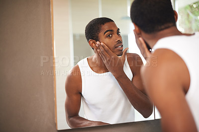 Buy stock photo A young man applying cream to his face while looking in the mirror