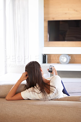 Buy stock photo Shot of a young woman changing channels with a remote control while relaxing on the couch