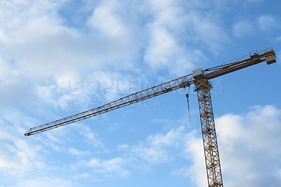 Buy stock photo Crane, outdoor and clouds or blue sky background for building with heavy machinery or construction material. Hoist in city, urban or industrial development with low angle, tools or overhead equipment