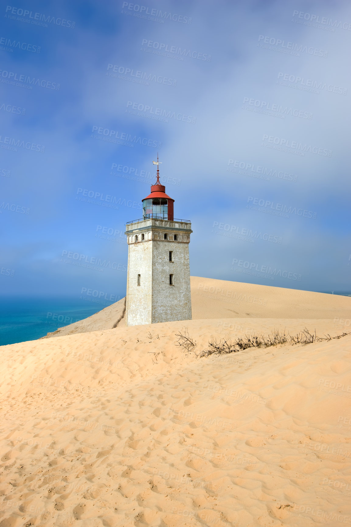 Buy stock photo Deserted lighthouse by the sea with blue sky in the background on a sunny day. A lighthouse in between the sandy area surrounded by water and cloudy sky. The mysterious old tower alone in the desert
