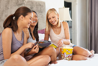 Buy stock photo Friends, popcorn and reading magazine on bed with laughing, discussion and girls night in home with pyjamas. Women, snack and happiness with paper in house for bonding, conversation and excited