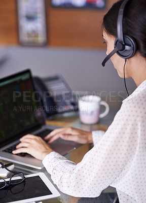 Buy stock photo Shot of an attractive young businesswoman working on a laptop while wearing a headset