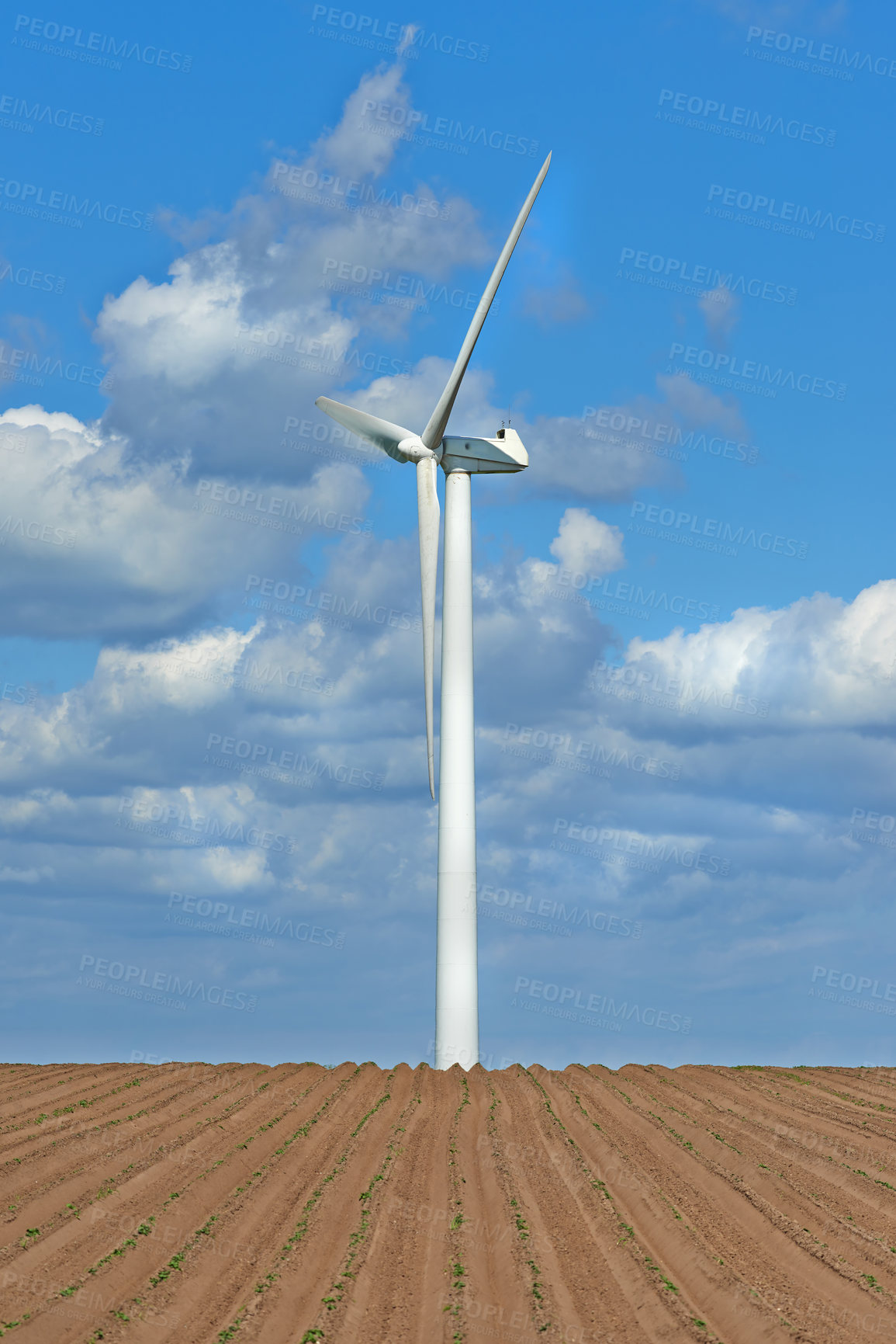 Buy stock photo Wind turbines on a farm with newly planted crops. Cloudy day on agricultural land where wind energy is the main resource. Producing sustainable electricity and fresh produce