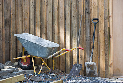 Buy stock photo A wheelbarrow and spade placed amongst gravel and building material. Construction site at a home in the backyard. Equipment and tools used to build a house. A shovel and other building equipment
