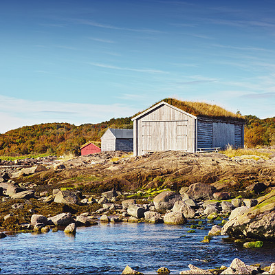 Buy stock photo Norway, house and outdoor in field, lake and rocks for travel and holiday in background with hills. Shed, grass and blue sky for cottage, serenity and sunlight for nature in season for  countryside