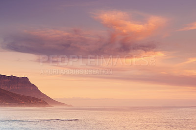 Buy stock photo Ocean, sunset and calm water by mountain and tourism destination for summer vacation in nature. Blue sky, clouds and neon color on cape town beach, peace and outdoor travel with sunshine in paradise