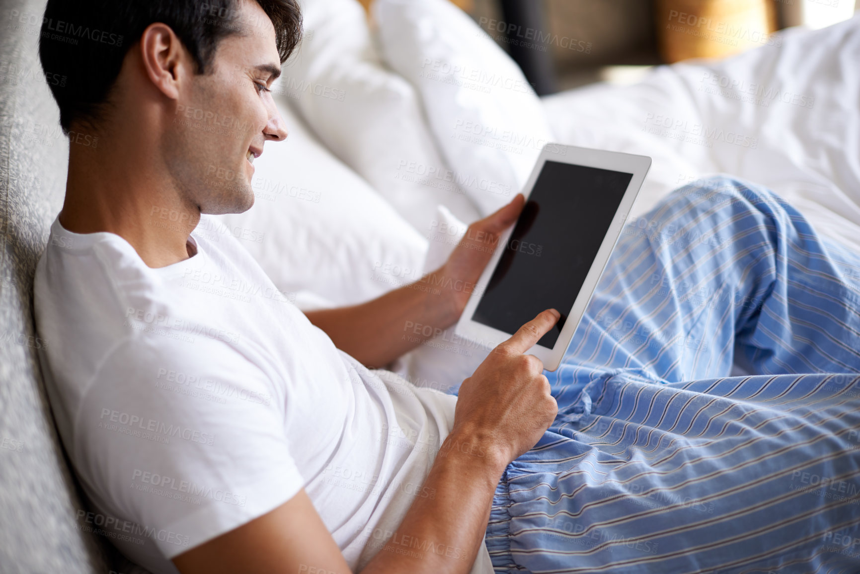 Buy stock photo Cropped shot of a handsome young man using his tablet in bed