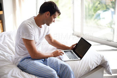 Buy stock photo Cropped shot of a handsome young man using a laptop on the edge of his bed