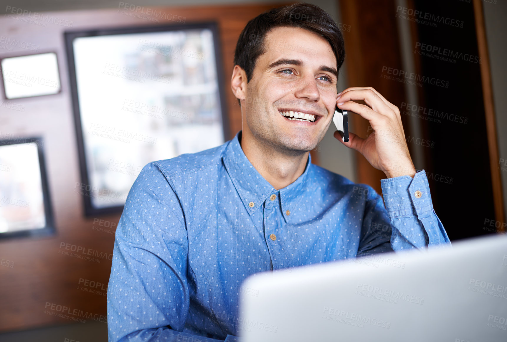 Buy stock photo Shot of a young businessman talking on the phone while sitting in front of his laptop