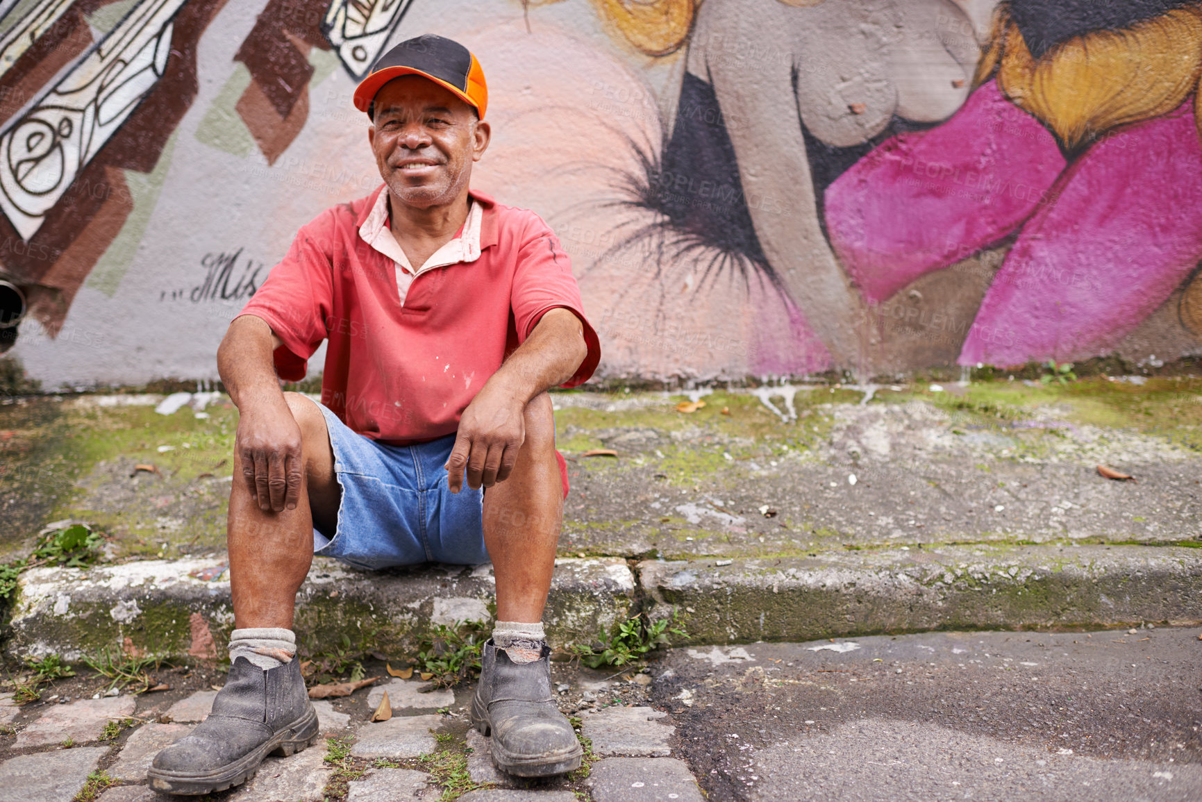 Buy stock photo Homeless, man and poverty in street, mature male person and graffiti art on wall in urban area. Smile, sitting and sidewalk in neighbourhood, third world or creative design in community for relax
