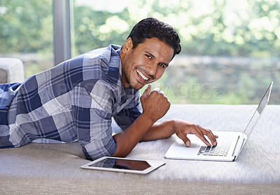Buy stock photo A young man using his laptop with his digital tablet lying next to him