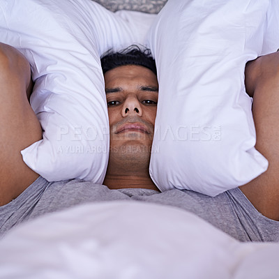Buy stock photo A young man covering his ears with his pillow