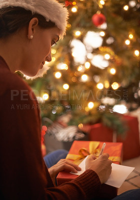 Buy stock photo Woman, writing letter and Christmas in home by tree, present and santa hat with message for festive wish. Girl, person and paper with notes, gift and package with kindness, celebration and xmas card