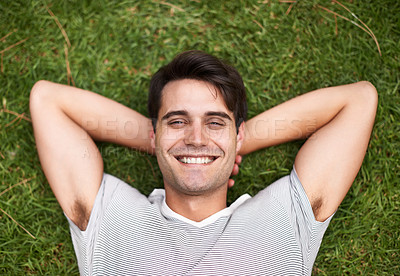 Buy stock photo Above portrait of one handsome young man lying with his hands behind his head at the park. Carefree male looking content while relaxing on the grass outdoors and enjoying his free time. Weekend vibes