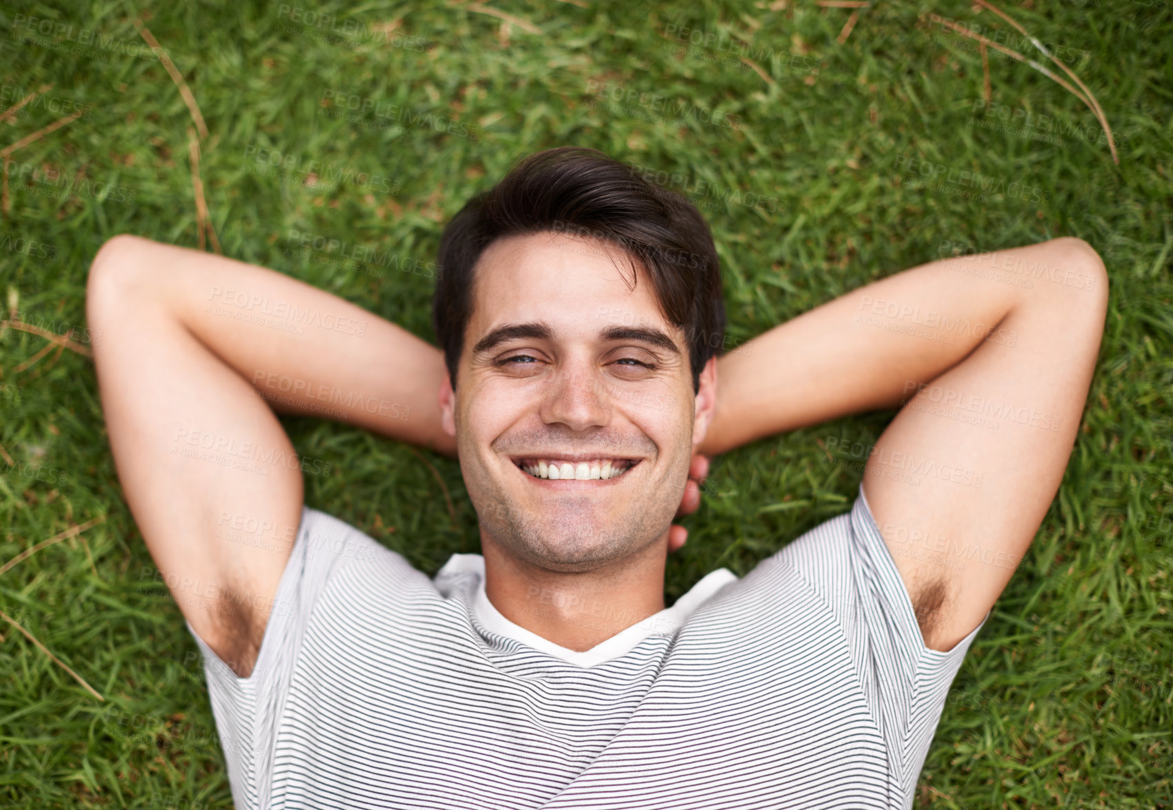 Buy stock photo Above portrait of one handsome young man lying with his hands behind his head at the park. Carefree male looking content while relaxing on the grass outdoors and enjoying his free time. Weekend vibes