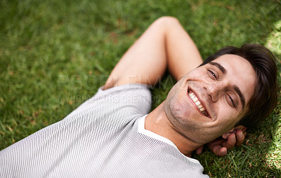 Buy stock photo Above portrait of one handsome young man lying with his hands behind his head at the park. Carefree male looking content while relaxing on the grass outdoors and enjoying his free time. Weekend vibes