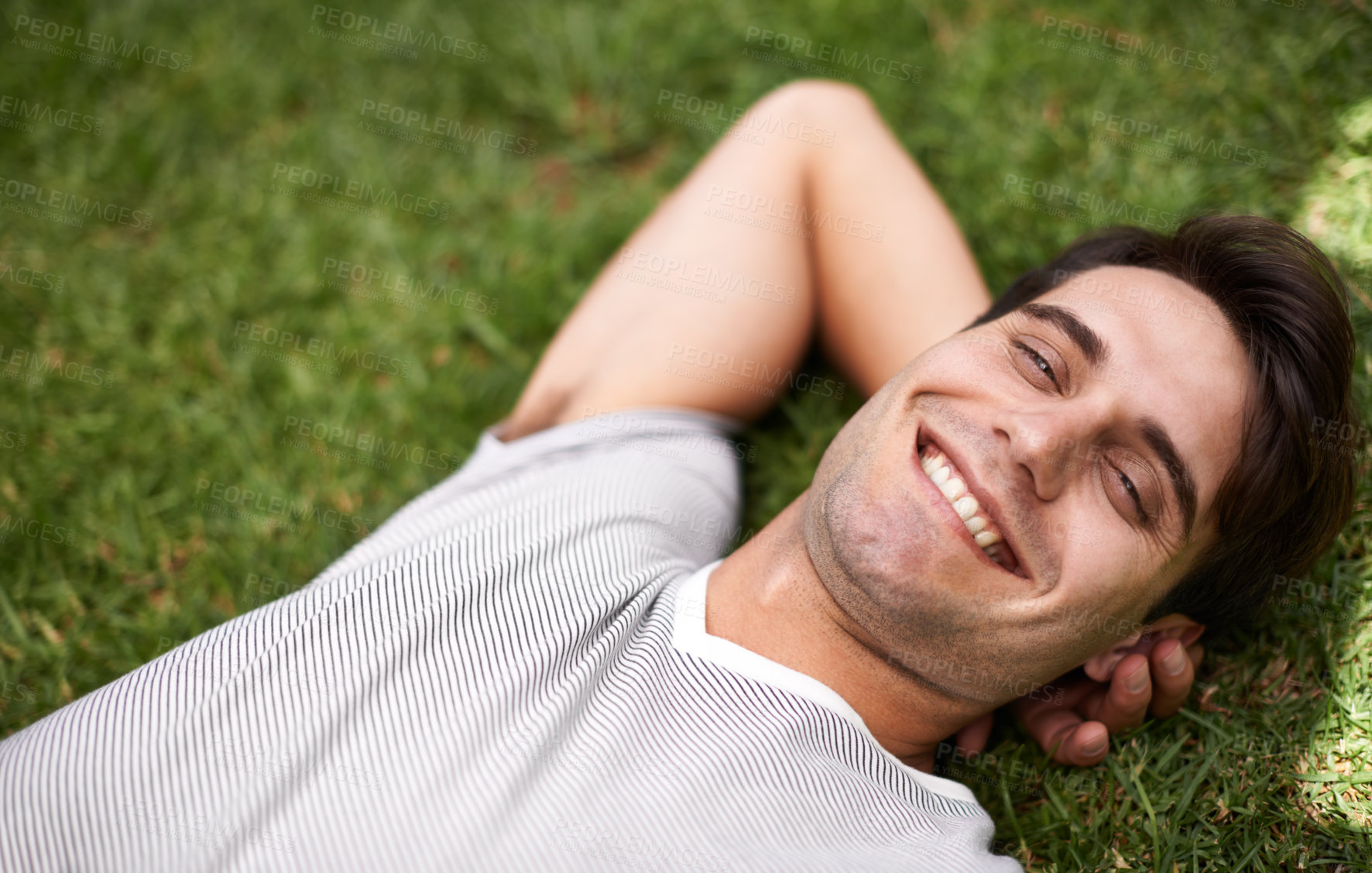 Buy stock photo Above portrait of one handsome young man lying with his hands behind his head at the park. Carefree male looking content while relaxing on the grass outdoors and enjoying his free time. Weekend vibes