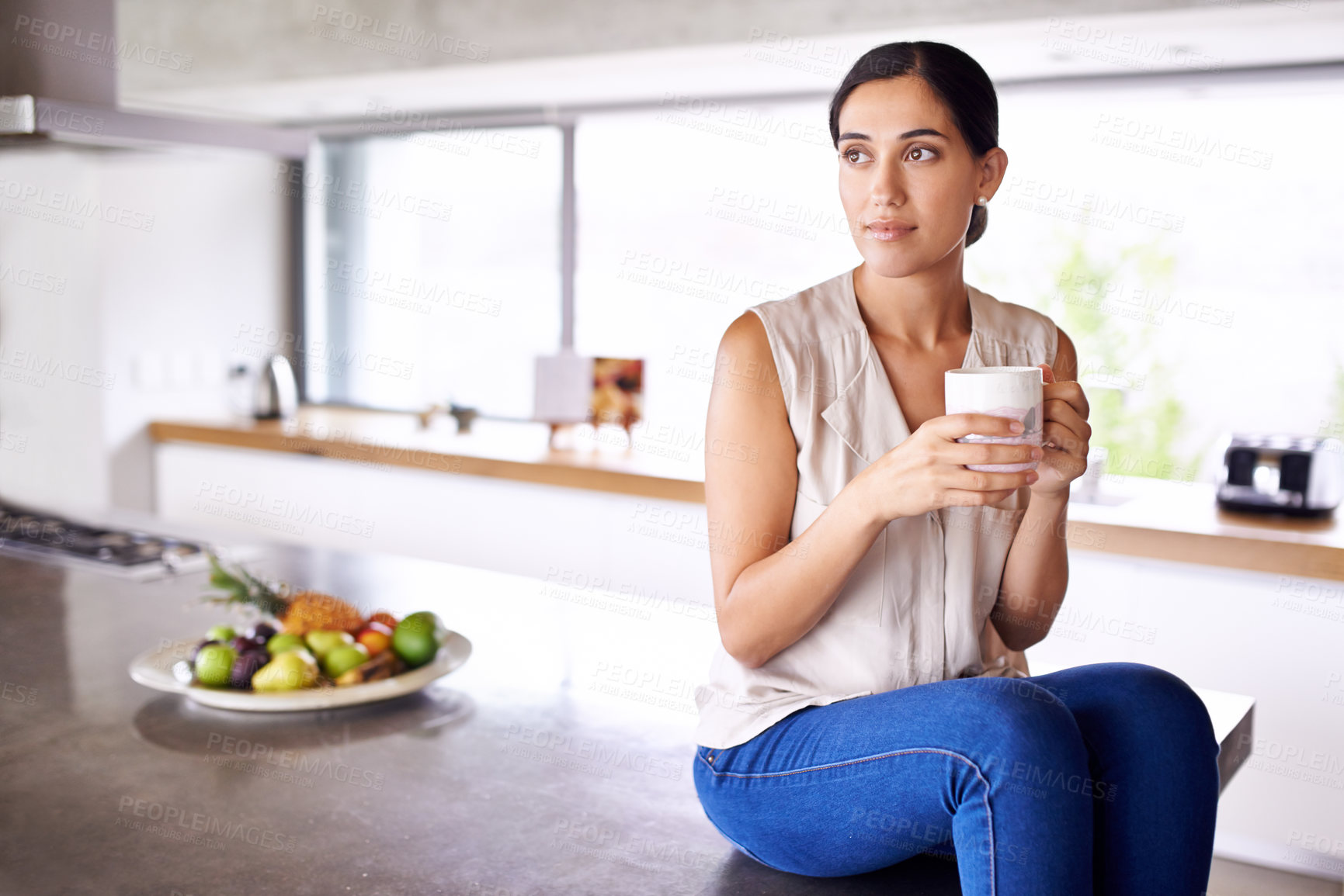 Buy stock photo Shot of an attractive young woman sitting on her kitchen counter and drinking coffee