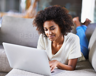 Buy stock photo Shot of a young woman using a laptop while relaxing at home on the couch