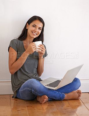 Buy stock photo Shot of a young woman sitting on the floor at home drinking a coffee and using a laptop