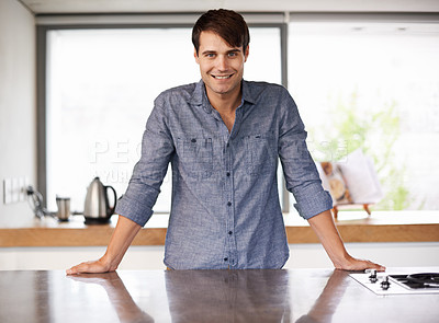 Buy stock photo Portrait of a handsome young man standing behind his kitchen countertop